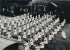 多摩製糸所の女工らが結成した国防婦人会の体操のようすで、作業用の割烹着に襷がけをしています。多摩製糸所は片倉製糸の工場で市内熊川にありましたが、戦時中は生糸生産が中止され、飛行機部品を製造する軍需工場となりました。
